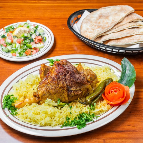 Middle-Eastern lamb shank with yellow rice, green peppers, tomato rose, salad, and pita bread.