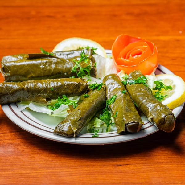 Plate of Jerusalem Restaurant's dolmas, garnished with parsley, lemon slices, and a carved tomato.