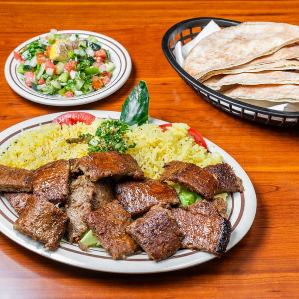 Middle-eastern dish with grilled meat, yellow rice, salad, and pita bread on a wooden table.